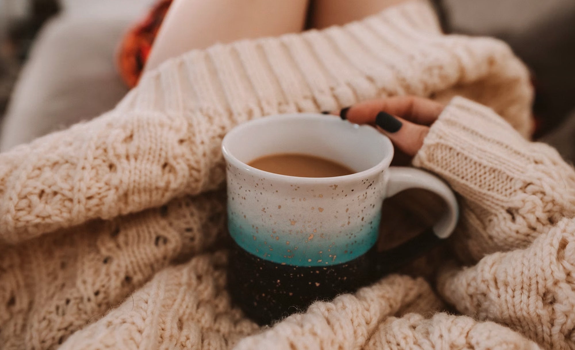 Immagine di una donna con un maglione di lana che tiene in mano una tazza di caffè